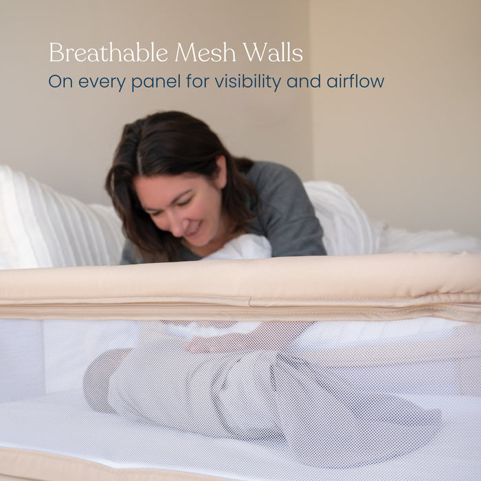 A woman smiles at a baby swaddled in the HALO 2-in-1 Bedside BassiNest Sleeper, which features breathable mesh walls on every panel for visibility and airflow.