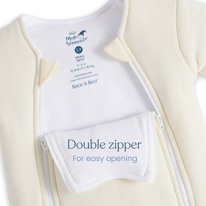 A close-up of the cream-colored HALO Baby Merlin's Magic Sleepsuit® 100% Cotton shows two open zippers, a white tag reading "Double zipper For easy opening," and an inner label with size info and the brand.