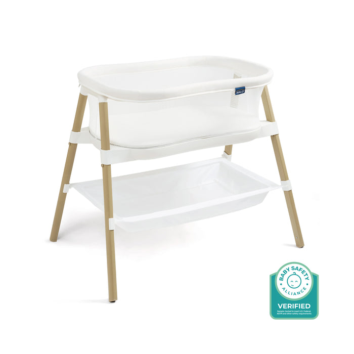 The HALO BassiNest® Essential Sleeper is a white mesh bassinet with wooden legs, mesh walls, a storage shelf underneath, and a space-saving design. A Baby Safety Alliance Verified badge appears in the bottom right corner.