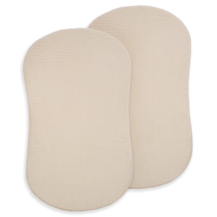 Two beige, oval-shaped BassiNest® Fitted Sheets by HALO overlap on a white background. Made from 100% organic cotton muslin, this 2-pack looks soft and breathable—ideal for a comfortable nursery.