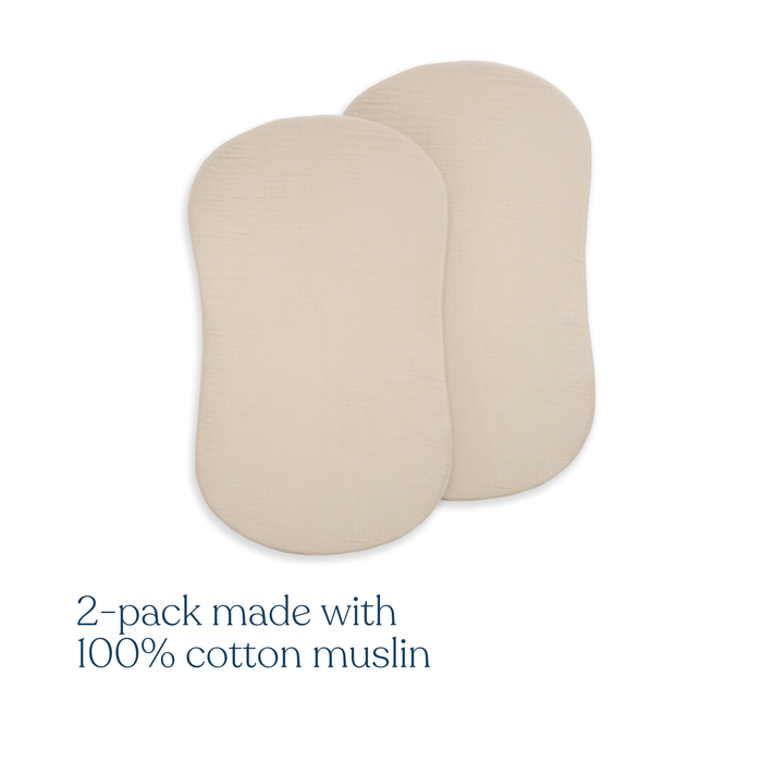 Two cream-colored, oval BassiNest® Fitted Sheets from HALO are shown overlapping. Text reads: 2-Pack made with 100% organic cotton muslin. Ideal for creating a breathable nursery environment.