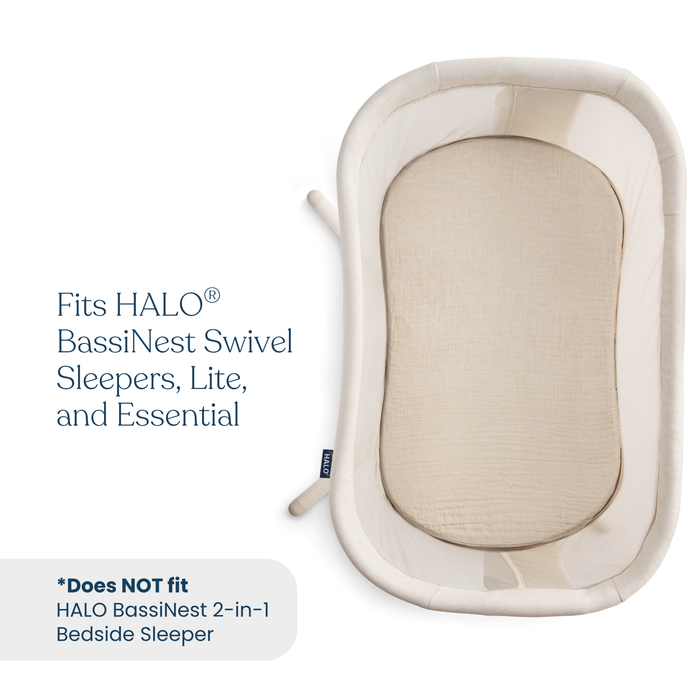 Top-down view of a beige, oval-shaped baby bassinet with mesh sides, featuring HALO BassiNest® Fitted Sheet 100% Organic Cotton Muslin 2-Pack. Compatible with BassiNest Swivel Sleepers, Lite, and Essential; not for 2-in-1 Bedside Sleeper.