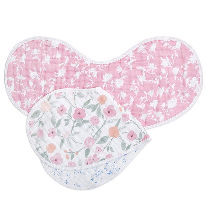 Displayed are two aden + anais Burpy Bibs. The top bib is pink with white floral patterns, and the bottom one has colorful flowers and green leaves on white. Crafted from absorbent 100% cotton muslin, both feature rounded edges and are folded to highlight their designs.