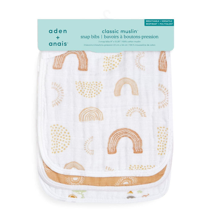 The aden + anais boutique 100% cotton muslin snap bibs 3 pack features a white and brown abstract pattern of rainbows and circles. These absorbent, breathable bibs offer an adjustable fit, with measurements provided in both centimeters and inches.