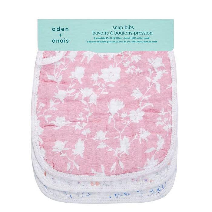 The aden + anais boutique 100% cotton muslin snap bibs 3 pack includes adjustable pastel pink and white bibs with floral patterns. Their absorbent design is highlighted by delicate white flower prints on the stacked pink bib in the packaging.