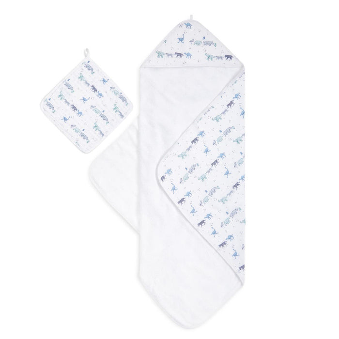 The aden + anais boutique 100% cotton oversized muslin backed towel + washcloth set showcases a delightful pattern of blue and green dinosaurs, with the towel and hood unfolded and the washcloth displayed above to reveal the matching designs.