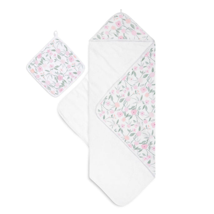 The aden + anais boutique set includes an oversized 100% cotton muslin-backed hooded towel and washcloth, adorned with a floral pattern in soft pink, peach, and green. Both pieces have convenient hanging loops.