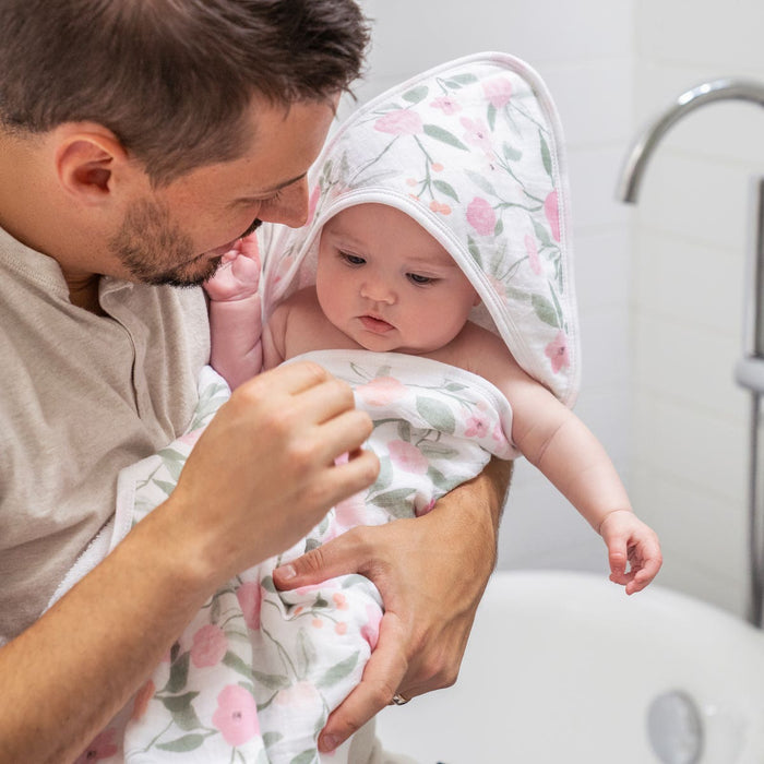 A man gently dries a baby wrapped in the HALO Mini Crib Essentials Bundle towel, sharing a tender moment in the bathroom after bath time. He smiles down at the baby, both enjoying this cozy bedtime essential.