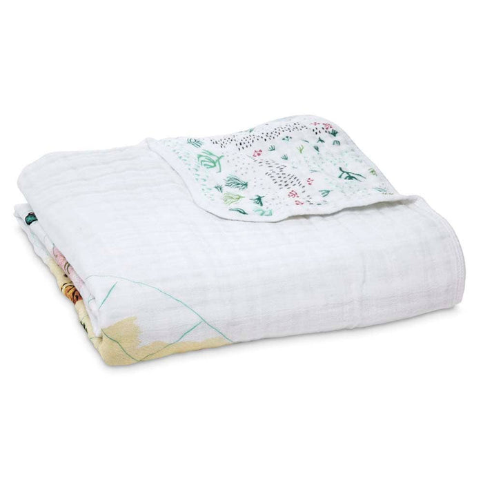 The aden + anais boutique cotton muslin dream blanket, crafted from 100% cotton muslin, highlights subtle tree and animal patterns. A corner displays a detailed leaf and tree design, offering a breathable and cozy feel that is extra soft and cuddly.
