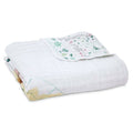 The aden + anais boutique cotton muslin dream blanket, crafted from 100% cotton muslin, highlights subtle tree and animal patterns. A corner displays a detailed leaf and tree design, offering a breathable and cozy feel that is extra soft and cuddly.