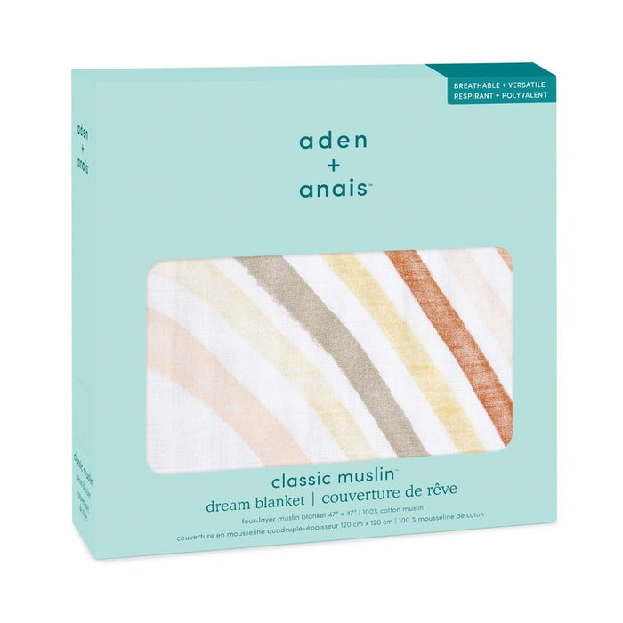 The image shows a boxed boutique cotton muslin dream blanket by aden + anais. The turquoise packaging has a window displaying pastel rainbow arcs, highlighting the blankets breathable and versatile attributes.