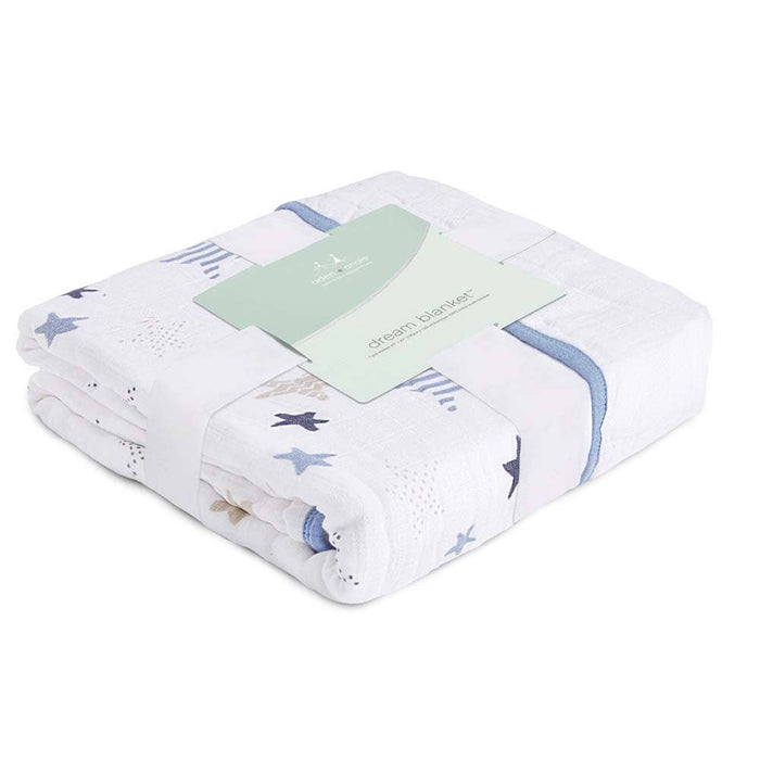 A folded boutique cotton muslin dream blanket by aden + anais, made from breathable cotton muslin and decorated with blue stars and dots, is elegantly wrapped in a white and light green paper label.