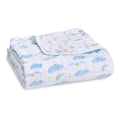 A boutique iconic cotton muslin dream blanket from aden + anais is neatly folded, showcasing a design with blue clouds and small golden suns. A flipped corner reveals a contrasting pattern of tiny animals and stars, reminiscent of the whimsical world of Harry Potter.
