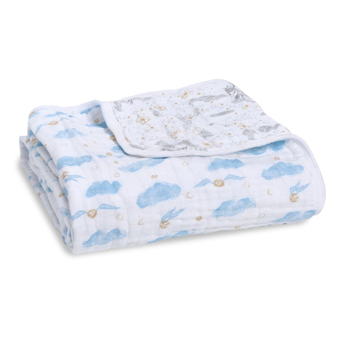 A boutique iconic cotton muslin dream blanket from aden + anais is neatly folded, showcasing a design with blue clouds and small golden suns. A flipped corner reveals a contrasting pattern of tiny animals and stars, reminiscent of the whimsical world of Harry Potter.