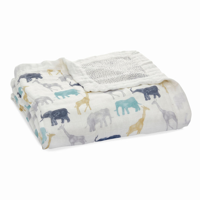The boutique silky soft muslin dream blanket by aden + anais is folded white with animal patterns, including elephants and giraffes, in blue, gray, and yellow. This ultra-smooth blanket features a textured gray square in one corner.