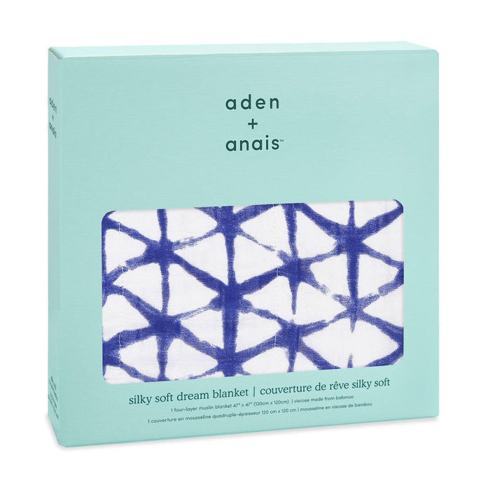 A box of aden + anais boutique silky soft muslin dream blanket comes in light blue packaging with a cutout showcasing the cozy, bamboo-infused treasure, featuring white fabric adorned with a bold blue geometric pattern.