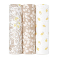 Three rolls of fabric stand upright: the left displays a bamboo-infused viscose with gray and yellow floral and animal patterns, the middle has a beige background with white leaves, and the right features an aden + anais boutique silky soft swaddle blanket on a white backdrop with yellow leaves.