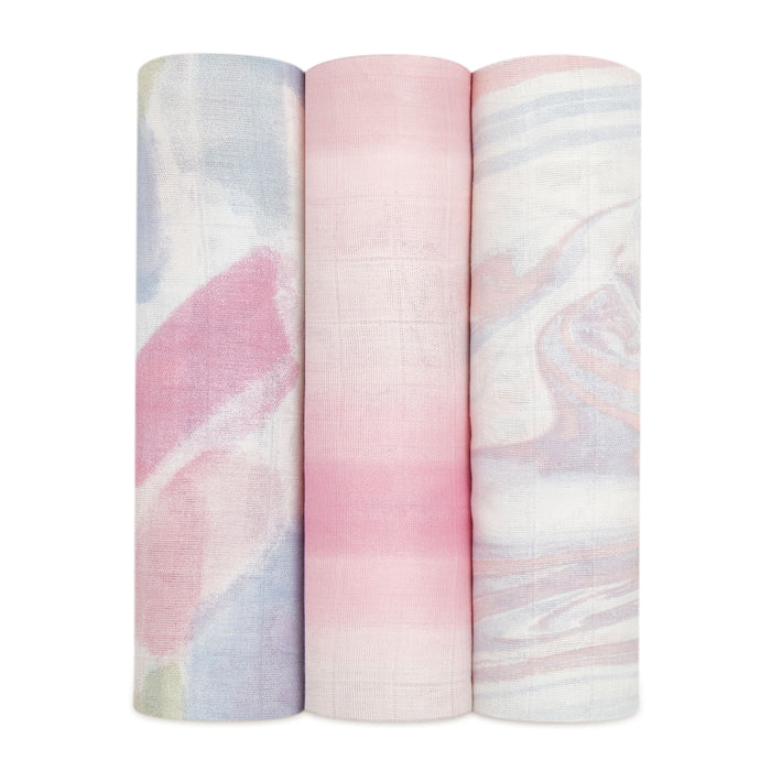 Three rolls of fabric from aden + anais stand together: the left with a pastel watercolor pattern, the middle in pink and white stripes, and the right with a swirling pink, white, and blue design. Crafted from bamboo-infused viscose, they are light and luxurious.