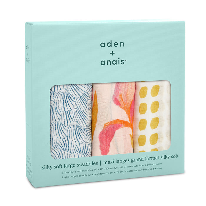 The aden + anais boutique silky soft swaddle blanket 3 pack includes bamboo-infused viscose swaddles in blue leaf, peach waves, and yellow dot designs. The turquoise box has a window showcasing the ultra-smooth large swaddles, offering silky softness for your baby.
