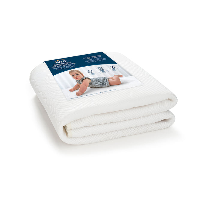 A white Breathable Crib Mattress Cover by HALO is folded and packaged with a label showcasing a baby on a bed, featuring HALO, DreamWeave, and icons for breathability, waterproof lining, and machine washable traits, ensuring comfort and convenience for your babys sleep environment.
