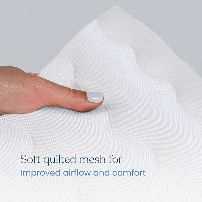 A hand with light nail polish presses into a white quilted fabric. Text reads, Soft quilted mesh for airflow and comfort. The HALO Breathable Crib Mattress Cover is machine washable, offering convenience and cleanliness.