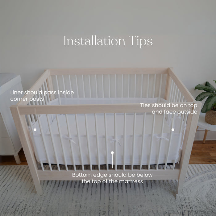 Image of a wooden crib with HALOs Breathable Mesh Crib Liner. Installation tips: pass the liner inside corner posts; ensure ties face outward on top, and position the bottom edge below the mattress top for optimal infant safety.