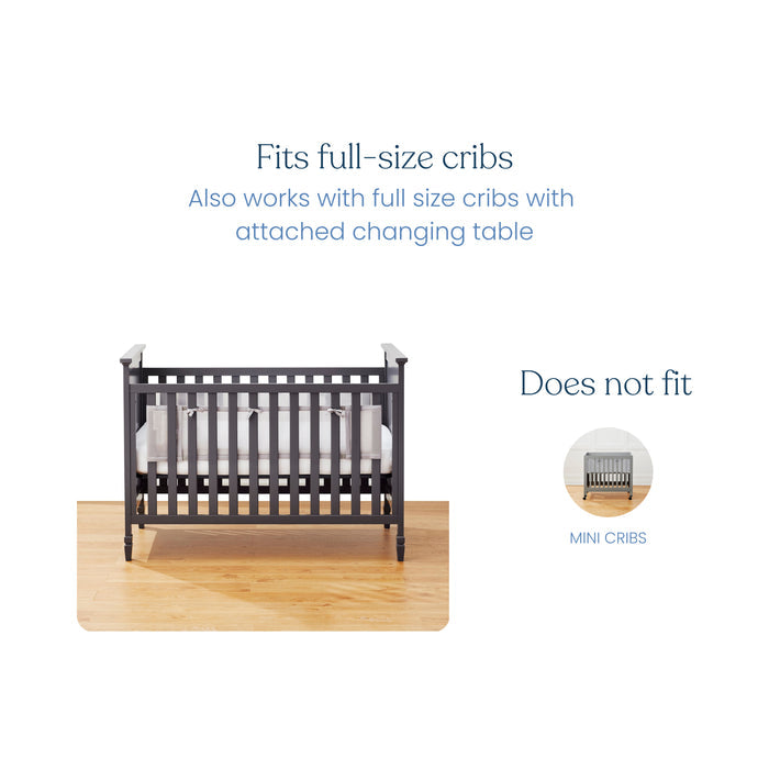 Image of a black full-size crib on a wooden floor with a mattress, ideal for the HALO Breathable Mesh Crib Liner for Full Sized Solid End Crib. This liner enhances infant safety and fits most full-size cribs, even with attached changing tables, but not mini cribs.