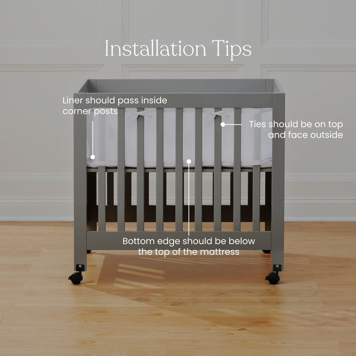 The HALO Breathable Mesh Crib Liner for Mini Cribs comes with these installation tips: ensure the liner passes inside corner posts, keep the bottom edge under the mattress top, and secure ties on top facing out. The setup on a wooden floor with a plain wall highlights crib safety.