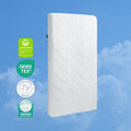 The HALO DreamWeave™ Breathable Crib Mattress stands upright against a blue sky with clouds, displaying four badges: GREENGUARD Gold, Oeko-Tex, Hypoallergenic Product, and Baby Safety Alliance Verified.