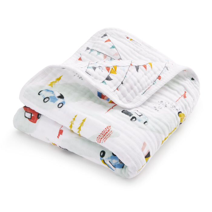 The aden + anais essentials cotton muslin dream blanket is a soft, quilted baby blanket with cozy, lightweight cotton muslin and colorful prints of cars, trees, and bunting flags.