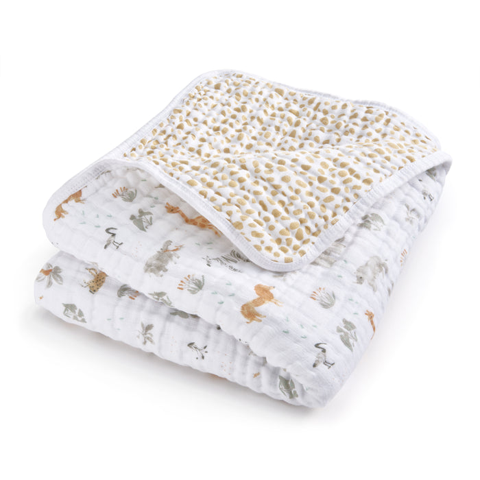 The essentials cotton muslin dream blanket by aden + anais is perfect for tummy time, featuring a cozy, enchanting animal and nature print with lions, turtles, and trees in muted hues. The reverse side has a delightful yellow scattered leaf pattern.