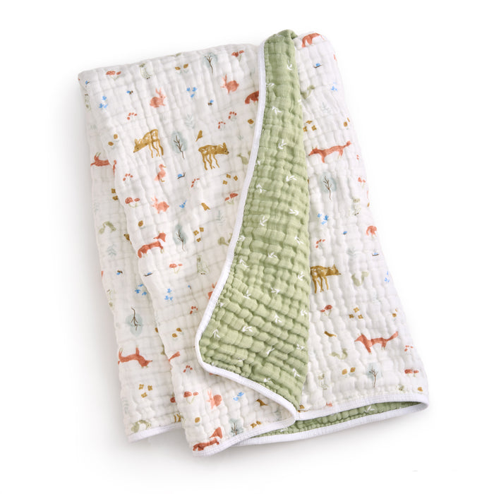 The essentials cotton muslin dream blanket by aden + anais features a playful animal design on the white side with giraffes and elephants, while the other side is solid green. This cozy, quilted baby blanket is crafted for warmth and comfort.