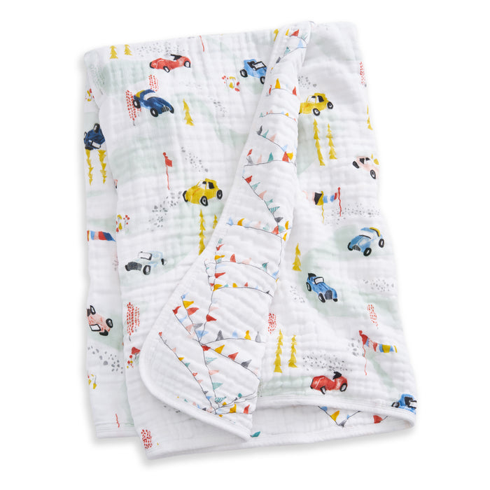 The aden + anais essentials cotton muslin dream blanket, made from soft cotton and featuring colorful cartoon cars, flags, and trees, is neatly folded to display part of its playful pattern.