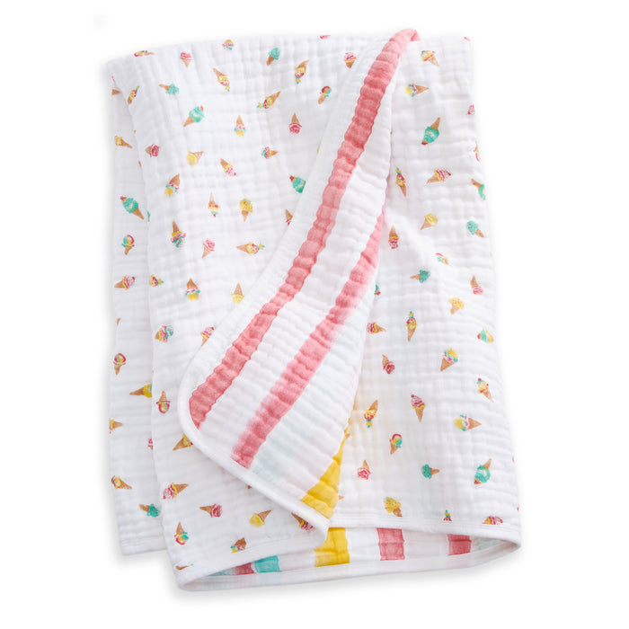 The aden + anais essentials cotton muslin dream blanket features colorful ice cream cone patterns and pastel striped trim in pink, yellow, and teal. The soft baby blanket is neatly folded with one corner flipped over.