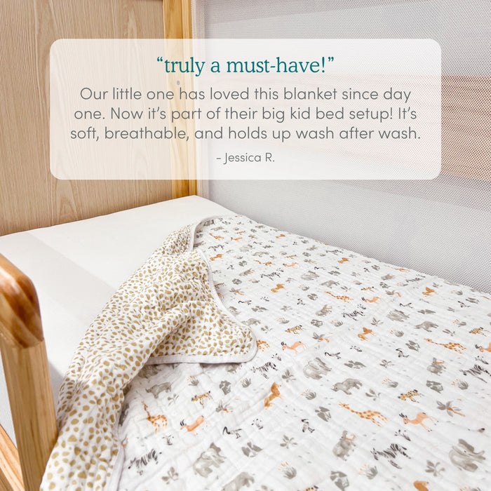 A white crib with light wood accents holds the aden + anais Disney™ Lilo and Stitch essentials cotton muslin dream blanket. A review hails this baby blanket as a “must-have” for its softness, breathability, durability, and long-lasting comfort.