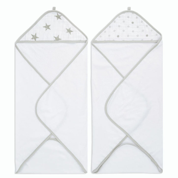 The aden + anais essentials cotton muslin hooded towels 2 pack includes two white plush cotton terry towels with gray edges. The left towels muslin hood has silver stars, and the right one features silver polka dots. Both are unfolded with hoods at the top.