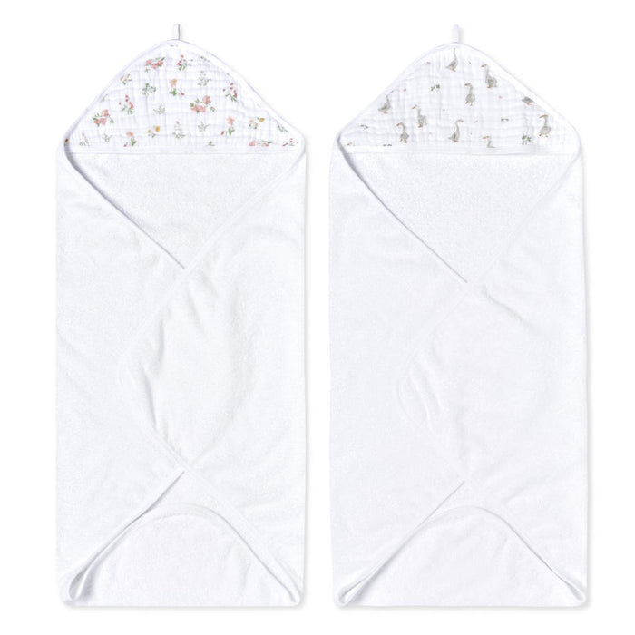 Two aden + anais essentials cotton muslin hooded towels are featured, each absorbent and plush. One towel has a pink floral lining and the other with gray animal patterns, both laid flat with hoods at the top.