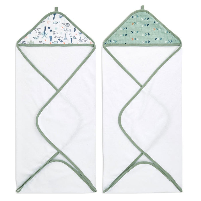 The aden + anais essentials cotton muslin hooded towels 2-pack features two white towels with green trim, crafted from plush cotton terry. One has a wildlife pattern on the hood, the other has stylized arrows, both super absorbent with hanging loops for convenience.