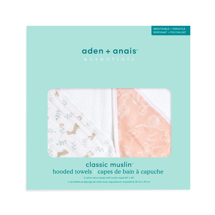 The aden + anais essentials cotton muslin hooded towels 2 pack includes two super absorbent cotton terry towels: one has floral designs on an orange background, and the other features animal patterns on a white backdrop. The turquoise box provides detailed product information.