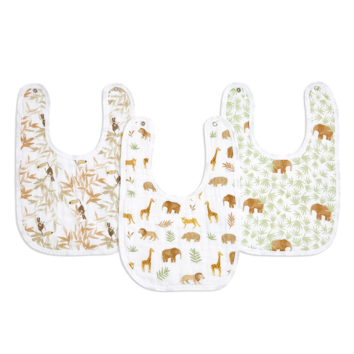 The essentials cotton muslin snap bibs 3 pack by aden + anais includes three triple-layered, absorbent bibs: one with tan bamboo leaves, one with elephants and giraffes, and one showing brown elephants on green leaves, all featuring white borders and snap closures.