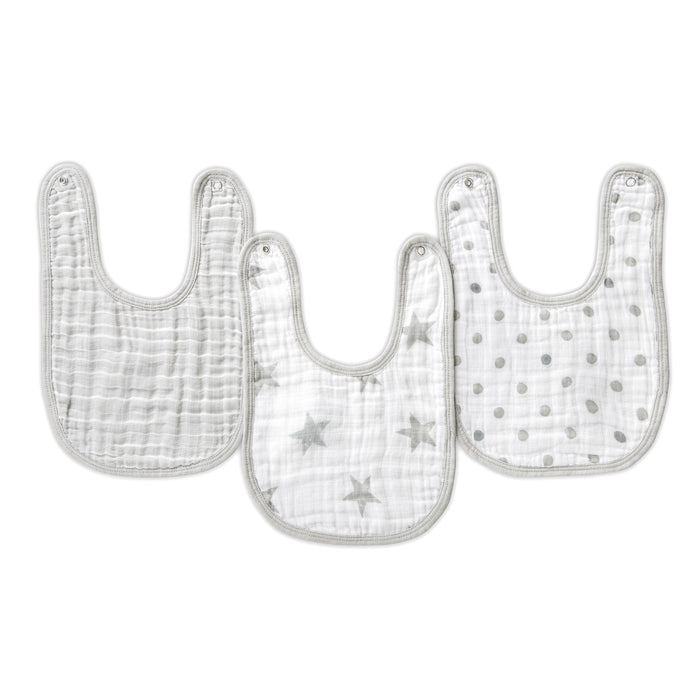 Three essentials cotton muslin snap bibs from aden + anais are shown, crafted from absorbent cotton muslin. Each light-colored bib has gray trims: one is plain, another with gray stars, and the third has gray polka dots, designed for growing convenience and comfort.