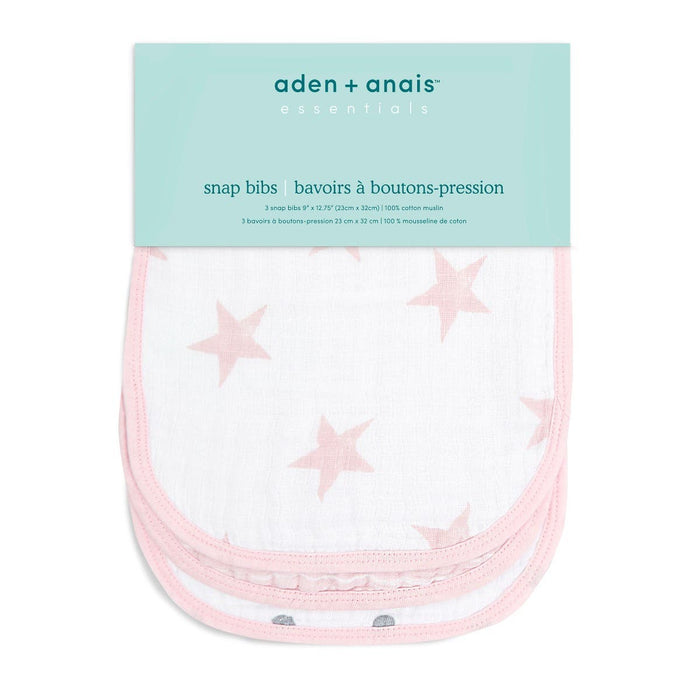A pack of three aden + anais essentials cotton muslin snap bibs is shown. These durable, absorbent bibs are white with light pink star patterns and a pink border. They come packaged under a turquoise label featuring the brand name and product description.