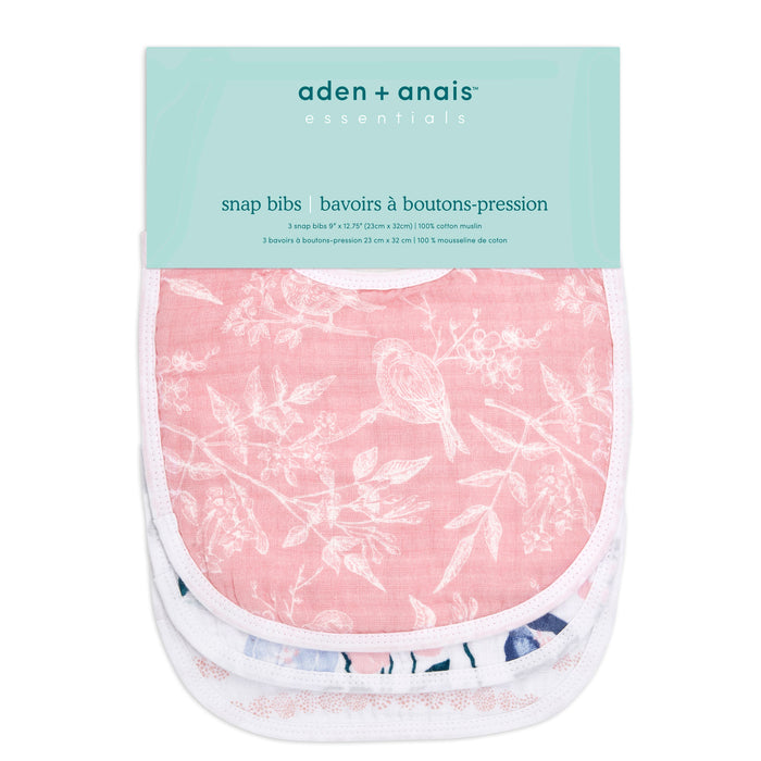 The essentials cotton muslin snap bibs 3 pack by aden + anais includes durable pastel-colored bibs, featuring a pink bib adorned with a white bird and floral pattern. Made from absorbent cotton muslin, the packaging displays the brand name and product details.
