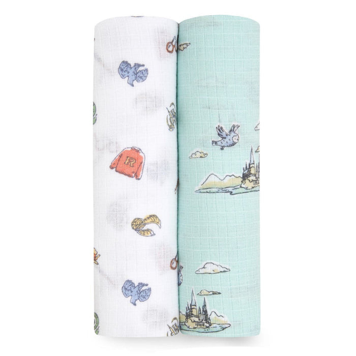 Two aden + anais essentials cotton muslin swaddle blankets are pictured. The left is white with colorful Harry Potter prints like mittens and a R sweater, while the right is light blue featuring sketches of a castle, clouds, and birds. Both are made from cozy cotton muslin.