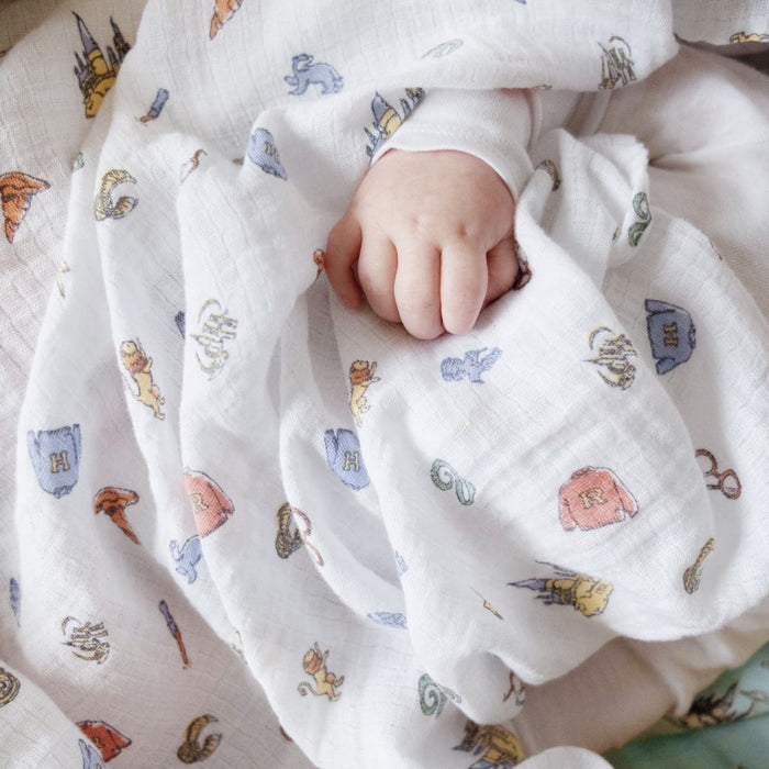 A babys hand gently grips the aden + anais essentials cotton muslin swaddle blanket, adorned with colorful, whimsical embroidered images in shades of blue, orange, and pink—ideal Harry Potter essentials for little dreamers.