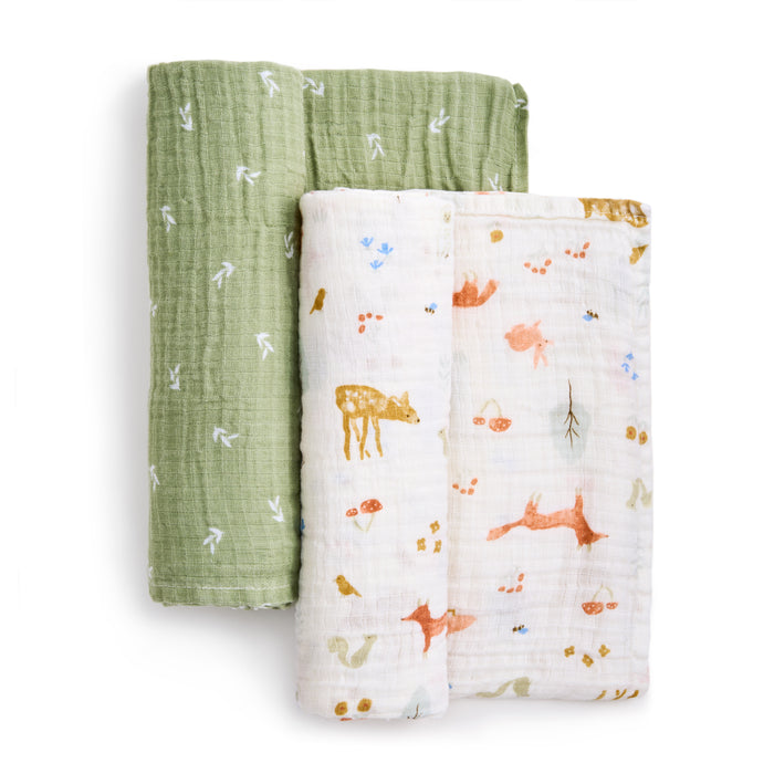 The aden + anais essentials cotton muslin swaddle blanket 2 pack is displayed. One swaddle features breathable green cotton muslin with white arrows, while the other showcases a white background with a colorful animal and leaf pattern.