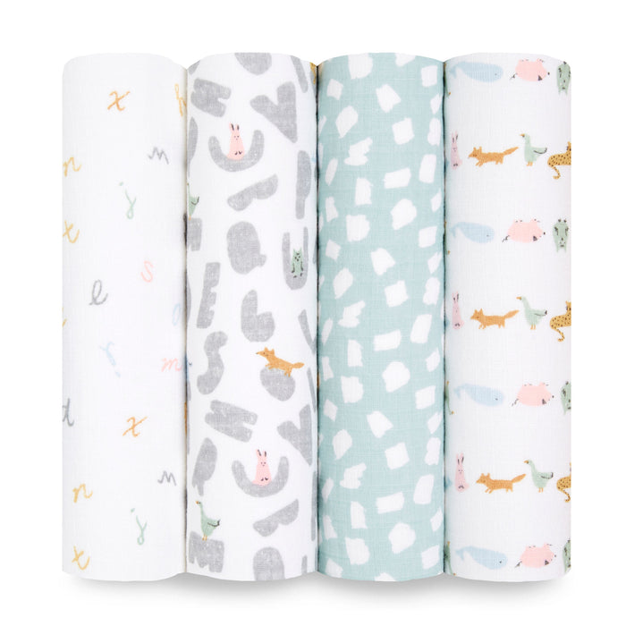 Four vertically rolled aden + anais essentials cotton muslin swaddle blankets showcase: multicolored alphabets, abstract gray shapes with little animals, a turquoise pattern with white designs, and pastel-colored scenic animals—all crafted from breathable cotton muslin.