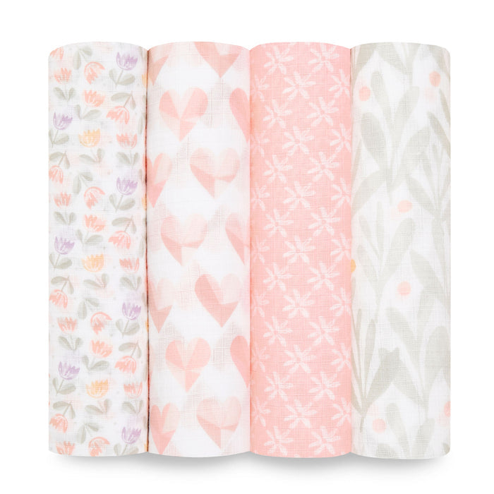 Displayed are four rolls from the aden + anais essentials cotton muslin swaddle blanket 4 pack: multicolored tulips, pink hearts, white stars on pink, and green leaves with orange dots. These soft, pastel-toned designs are crafted from breathable cotton muslin.