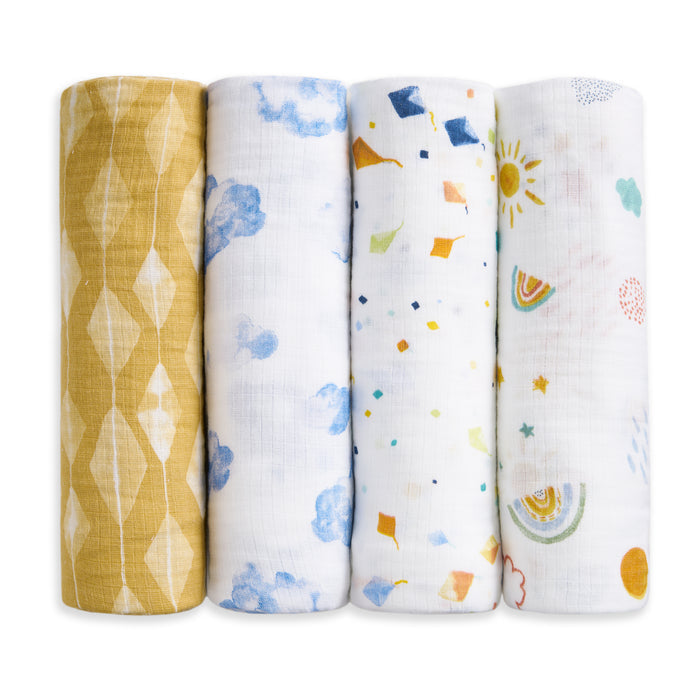 Four aden + anais essentials cotton muslin swaddle blankets stand upright, each with a distinct pattern: yellow diamonds, blue watercolor clouds, colorful confetti, and rainbows with suns on white.