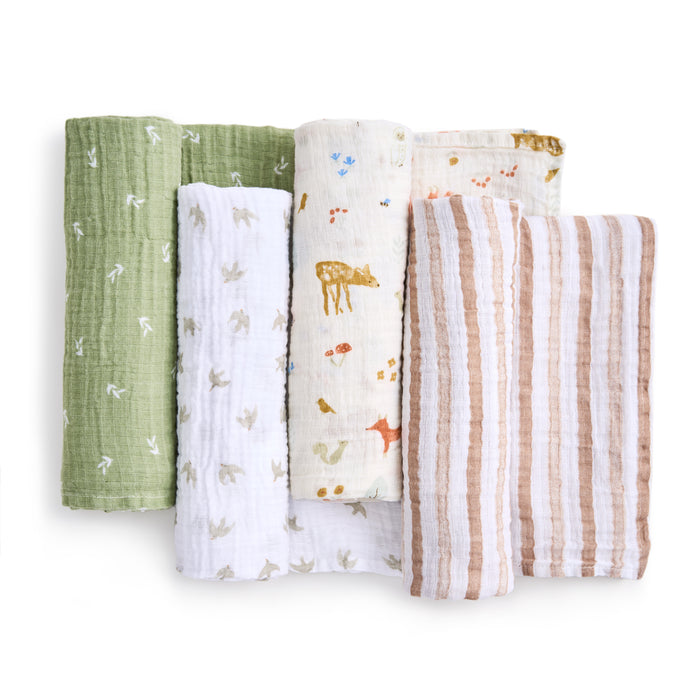 Four versatile aden + anais essentials cotton muslin swaddles are displayed upright: a green one with white birds, a white one with gray patterns, another white adorned with animal designs, and a brown one accented by white stripes.